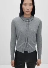 Cárdigan gris de punto fino con cuello redondo y cierre frontal con botones. Tiene costuras decorativas en negro en cuello, botones y borde frontal.