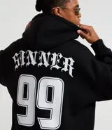 Hoodie negro de corte boxy, con capucha ajustable, bolsillo canguro y detalles bordados en el pecho. Presenta un estampado grande en la parte frontal con tipografía gótica y texto en dorado.