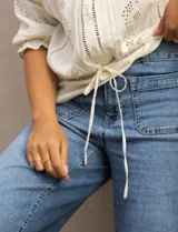 Blusa color crema con cuello redondo, abertura central con botones y mangas 3/4 con puño fruncido. Presenta detalles calados y bordados en mangas, delantera y espalda. La cintura se ajusta con un lazo.