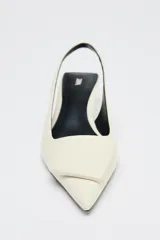 Zapato destalonado color crema con tacón fino y adorno en la parte delantera.