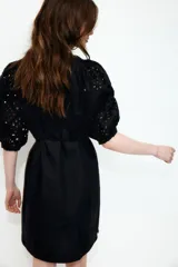 Vestido a la rodilla negro en tejido liviano de algodón con cuello redondo, botones ocultos adelante y cinturón para atar fino extraíble. Mangas al codo abullonadas en broderie con puños elásticos.