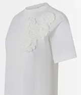 Blusa blanca de algodón con cuello redondo, mangas cortas y apliques de flores de tela en el hombro.