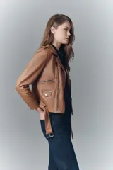 Campera negra de cuero ovino, estilo rocker, con cinturón, charreteras y solapas. Tiene cierres y detalles metálicos en frente y espalda.