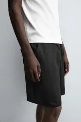 Bermuda negra de corte relajado, confeccionada en tejido satinado de viscosa. Presenta cintura elástica ajustable con cordón interior, bolsillos frontales y un bolsillo trasero de plastrón.