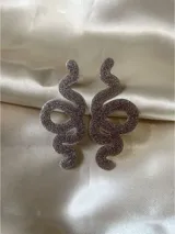 Par de aros colgantes con forma de serpiente, color negro con glitter. Cierre a presión de acero inoxidable.