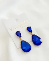 Aros colgantes dorados con dos piedras facetadas azules en forma de lágrima.
