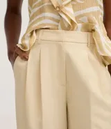 Pantalón de vestir de mujer, tiro alto, corte wide leg, color beige claro. Presenta pliegues frontales y frisos marcados.