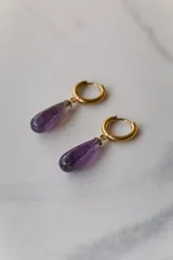 Aros colgantes con argolla dorada de acero quirúrgico hipoalergénico y dije de piedra natural color violeta en forma de gota.