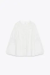 Camisa blanca de cuello redondo y manga larga con bordados combinados a tono y cierre frontal con botones.