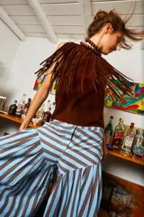 Gargantilla de cuero marrón con flecos y cierre con lazo. El collar de esferas marrones que se ve en la imagen es solo para estilismo.