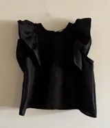 Blusa negra de lino con volados en los hombros y pespuntes en color beige.