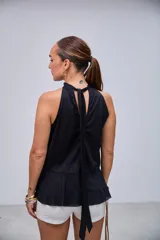 Blusa negra con cuello halter y escote en V, adornada con volados en el frente y en el bajo. Diseño asimétrico y tiras largas que caen por la espalda.
