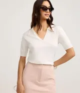 Blusa de punto color blanco, con cuello polo, escote en V y mangas cortas. Detalle de mini perlas aplicadas en el cuello.