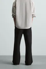 Pantalón negro de algodón con corte relajado y pierna ancha (flare fit). Presenta cierre frontal con botón y cremallera, bolsillos delanteros y bolsillos traseros de plastrón.