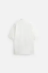 Polo blanco de piqué con corte relaxed fit, cuello solapa y cierre frontal con botones.