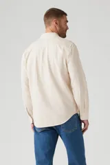 Camisa de manga larga color crema, con cuello clásico, cierre frontal con botones y bolsillo de parche en el pecho izquierdo con logo de la marca.