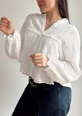 Camisa blanca de muselina con cuello en V, mangas largas con puños elásticos y detalle de bordado en el canesú.