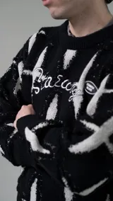 Sweater de punto negro con diseño de cruces blancas, cuello redondo y bordado con la palabra "Starrr" en el pecho.
