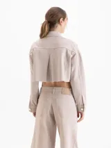Chaqueta corta estilo jeanero, color beige claro, confeccionada en algodón. Presenta botones metálicos y remaches decorativos en el cuello.