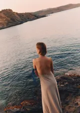 Vestido largo color beige, con cuello halter cruzado y espalda abierta. Diseño evasé.