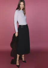 Falda midi plisada negra, de tiro alto, con doble cinturón de cuero sintético con hebillas plateadas.