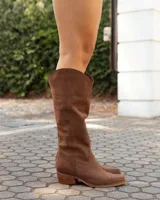 Botas texanas de caña media confeccionadas en cuero gamuzado color marrón. Presentan un diseño de corte clásico con costuras decorativas en el empeine, puntera levemente redondeada y taco bajo de madera.