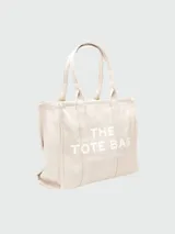 Bolso tote negro de lona con asas cortas y estampado frontal en letras blancas con la leyenda "THE TOTE BAG MARC JACOBS".