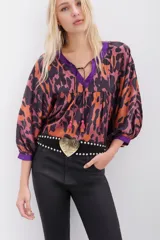Camisa de corte amplio con estampado animal print en tonos naranja, marrón y violeta, con escote en V con lazos para atar y mangas 3/4 abullonadas.