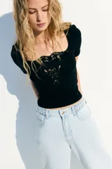 Top corto negro de punto suave con escote cuadrado amplio y bajo recto. Modelo de manga corta con ajuste entallado y detalle en V en broderie en el centro del busto.