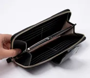 Billetera dorada con cierre metálico y solapa con el logo de la marca Vanitas. Tiene múltiples compartimentos para tarjetas y billetes. Incluye correa de muñeca extraíble.