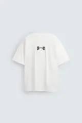 Camiseta blanca de corte holgado, cuello redondo y manga corta. Estampado frontal con texto en color negro y parche en la espalda. Detalle de pliegues en la espalda.