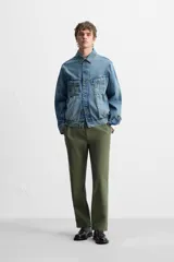 Pantalón chino color verde militar, de corte recto, con bolsillos laterales y traseros de vivo. Cierre frontal con cremallera y botón.