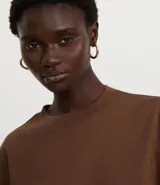 Blusa color beige, cropped y de corte amplio, confeccionada en tejido de media malla, con cuello redondo y mangas cortas.