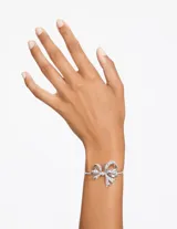 Brazalete rígido plateado con forma de lazo adornado con cristales transparentes.