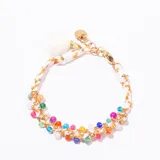 Pulsera tejida con hilo blanco y dorado, con pequeños dijes de cuentas de colores vibrantes y cierre de mosquetón dorado. Incluye un pequeño pompón blanco como detalle colgante.