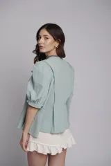 Chaqueta o blusa de tejido natural color verde menta, con mangas balloon y un botón decorativo en forma de estrella de mar. El cuerpo tiene un ruedo evasé.