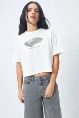 Remera cropped blanca de mangas ranglan con estampa frontal de un auto antiguo y texto "Vintage Gems / retro car club".