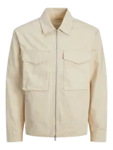 Chaqueta color crema, de manga larga, con cuello camisero y cierre frontal con cremallera metálica. Tiene dos bolsillos de parche con solapa en el pecho.