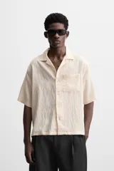 Camisa color crema de manga corta con cuello bowling, corte relaxed fit y bolsillo de parche en el pecho.
