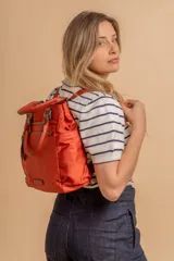 Mochila bandolera color marrón con herrajes color peltre. Tiene un compartimento principal amplio con cierre, un bolsillo frontal con cierre y dos bolsillos laterales abiertos. Incluye correa ajustable para usar al hombro o cruzada.