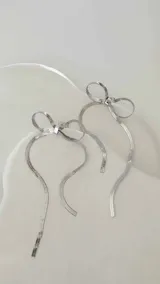 Par de caravanas plateadas con forma de moño y flecos.