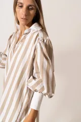 Camisa a rayas verticales color beige y blanco, de corte holgado, con cuello camisero y mangas largas abullonadas con puños abotonados.