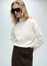 Sweater blanco de punto medio con cuello alto y cierre de cremallera en el hombro. Diseño recto, manga larga y terminaciones en canalé.