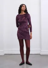 Conjunto de falda y top de terciopelo color borgoña con estampado floral en relieve. La falda es corta y drapeada. El top es de manga larga y cuello redondo.