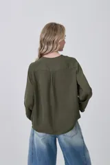 Blusa blanca de poliéster, entallada, con escote en V y botones frontales. Presenta mangas largas con puños anchos.