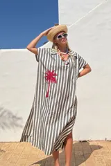 Túnica larga a rayas verticales blancas y negras, con cuello camisero, mangas cortas y bordado de una palmera roja en el frente.