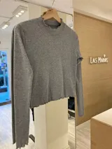 Remera gris de morley de algodón, de manga larga, con terminaciones fruncidas en cuello y mangas.