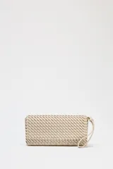 Bolso alargado color beige con diseño trenzado, asa bandolera y tirador con pulsera de mano. Incluye bolsillo interior y cierre mediante solapa y botón imantado.