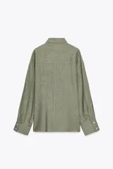 Camisa amplia color negro confeccionada con hilatura de lino. Tiene cuello solapa, manga larga, bolsillo de plastrón en el delantero, bajo asimétrico y cierre frontal con botones.