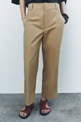 Pantalón color beige de corte ancho, con tiro medio, trabillas en la cintura y raya planchada.